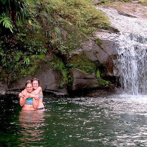Two women standing in water by a waterfall